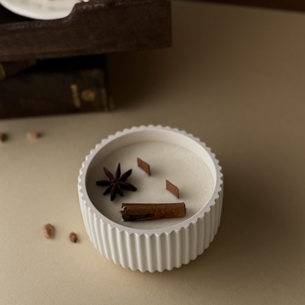 Vela_artesanal_resina_Chai_Latte Vela artesanal de Chai Latte decorada con anís y un palo de canela. Es una vela blanca en un recipiente blanco de resina con dos mechas de madera.